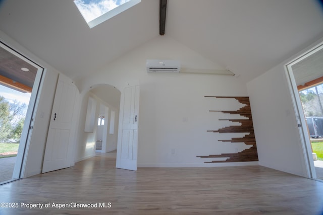 unfurnished room featuring a wall mounted air conditioner, a skylight, high vaulted ceiling, light hardwood / wood-style flooring, and beam ceiling