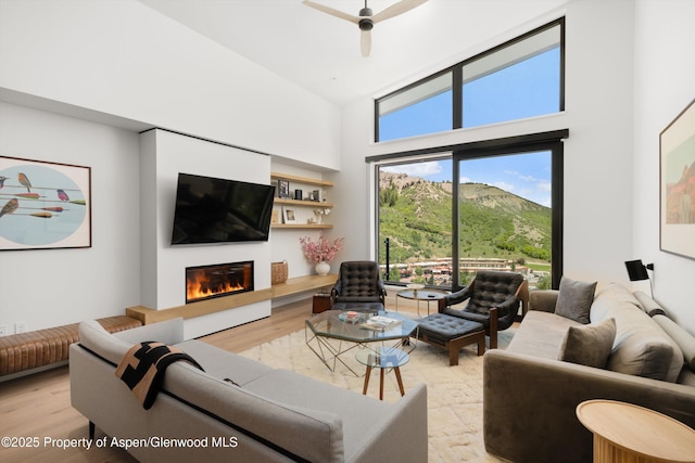 119 Wood Rd Unit 604, Snowmass Village, CO 81615 - living area featuring light wood-style floors, a towering ceiling, a glass covered fireplace, and ceiling fan