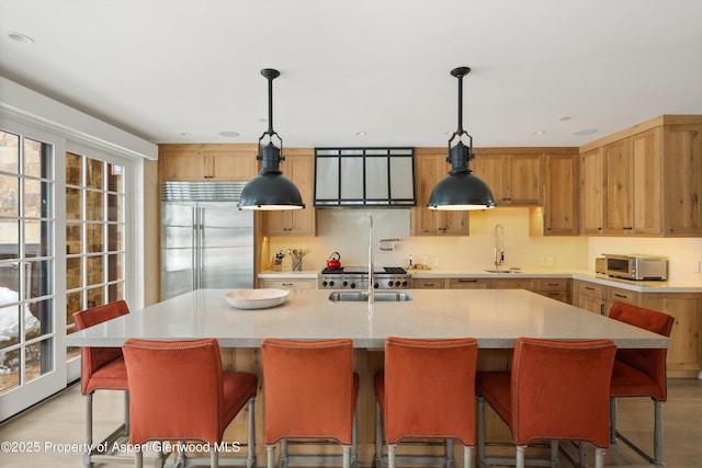 kitchen featuring built in fridge, a toaster, a sink, an island with sink, and decorative light fixtures