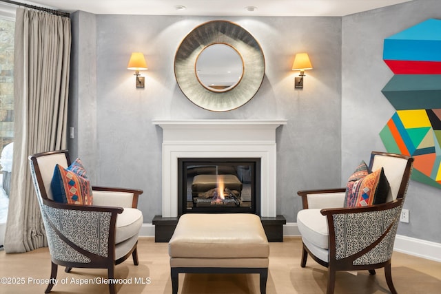 living area featuring baseboards, wood finished floors, and a glass covered fireplace