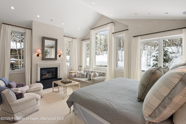 carpeted bedroom featuring a glass covered fireplace, multiple windows, vaulted ceiling, and recessed lighting