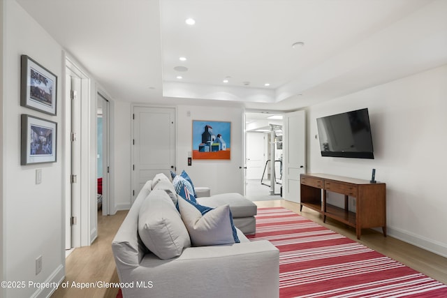 living area featuring baseboards, light wood-type flooring, a raised ceiling, and recessed lighting