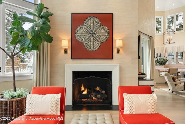 living area with a warm lit fireplace, a chandelier, a wealth of natural light, and wood finished floors