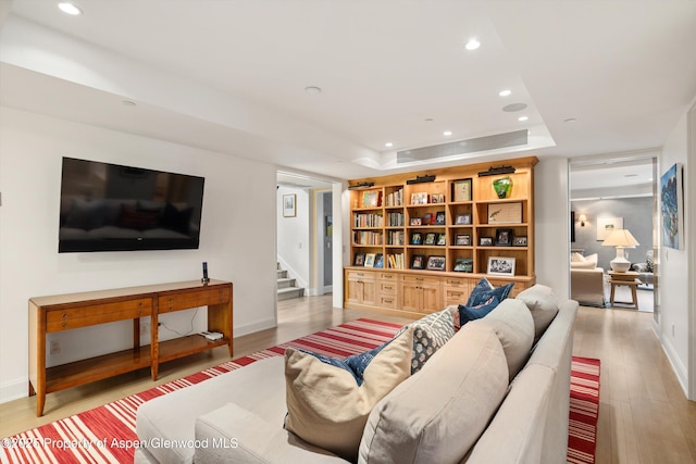 living room with stairs, a tray ceiling, light wood-style flooring, and recessed lighting