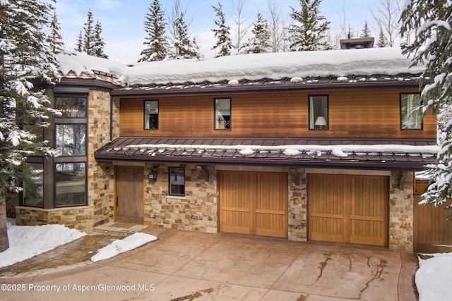 chalet / cabin featuring an attached garage, a standing seam roof, metal roof, stone siding, and driveway