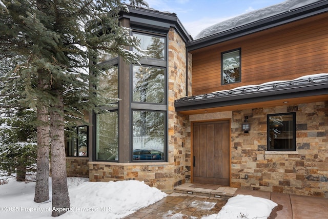 snow covered property entrance featuring stone siding