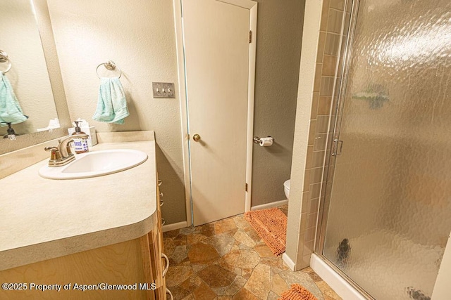 full bath featuring vanity, stone finish floor, toilet, and a shower stall