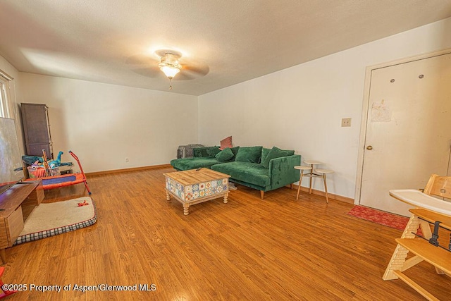 living area with baseboards, a ceiling fan, and wood finished floors