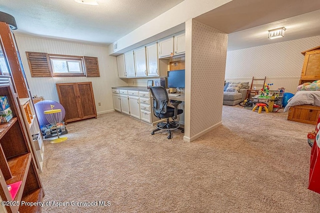 home office with light colored carpet, built in study area, wainscoting, and wallpapered walls