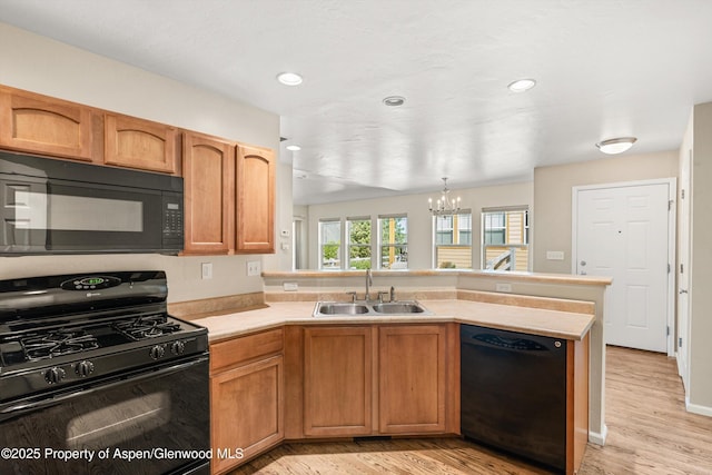 kitchen featuring black appliances, a sink, a peninsula, light countertops, and a chandelier