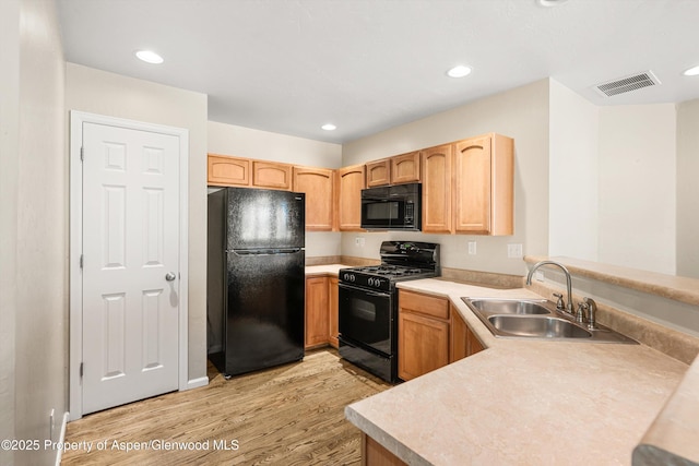 kitchen with black appliances, a sink, light wood-type flooring, light countertops, and a peninsula