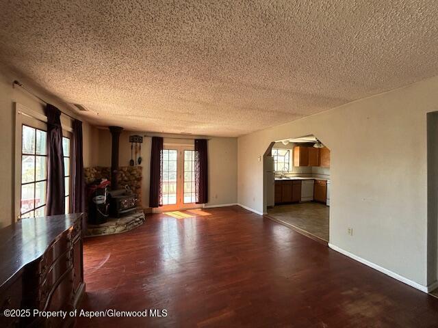 900 Breeze St, Craig, CO 81625 - unfurnished living room with a wood stove, baseboards, dark wood-style floors, a textured ceiling, and arched walkways