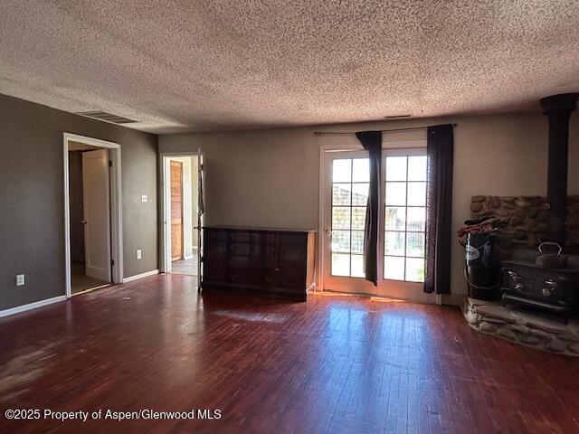 900 Breeze St, Craig, CO 81625 - unfurnished living room featuring a textured ceiling, visible vents, a wood stove, wood finished floors, and baseboards