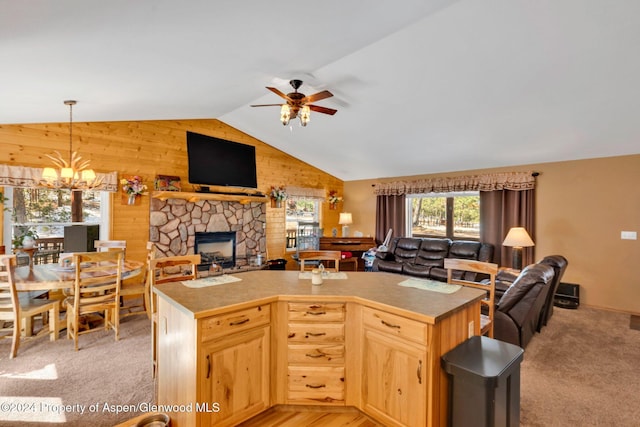 kitchen featuring light brown cabinetry, a stone fireplace, a center island with sink, and ceiling fan with notable chandelier