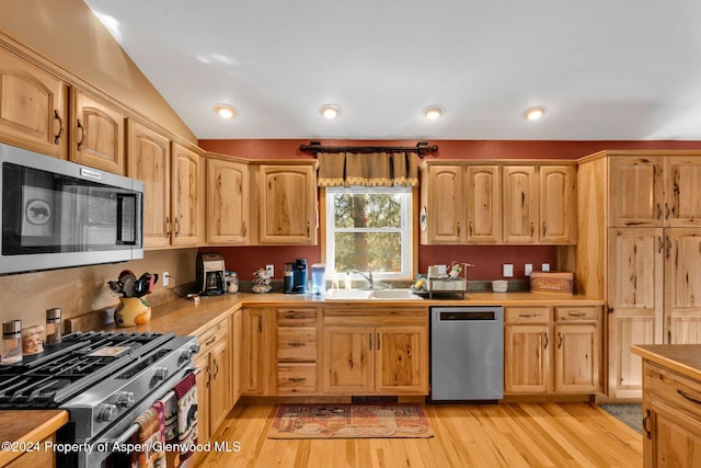 kitchen with appliances with stainless steel finishes, vaulted ceiling, light hardwood / wood-style flooring, and sink