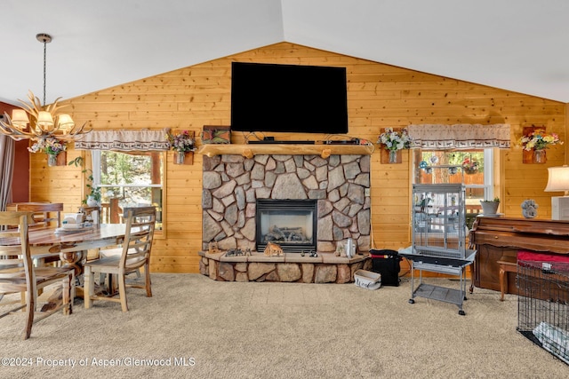 carpeted living room featuring a stone fireplace, wooden walls, vaulted ceiling, and an inviting chandelier