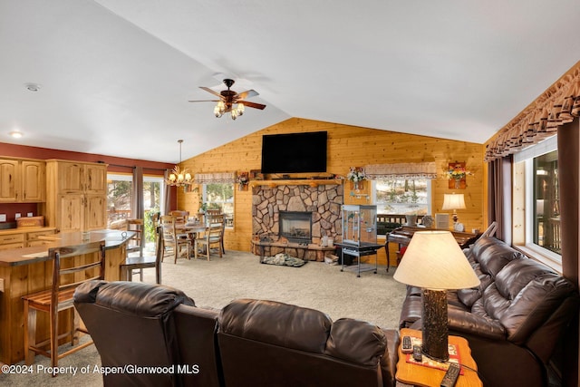 carpeted living room featuring lofted ceiling, a stone fireplace, wood walls, and ceiling fan with notable chandelier