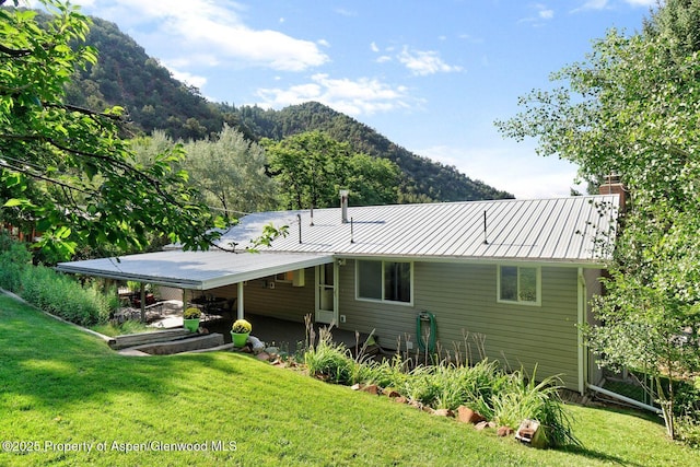 rear view of property with a lawn, a chimney, metal roof, a standing seam roof, and a mountain view