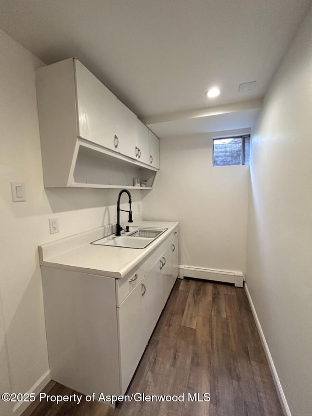 clothes washing area featuring dark wood-style floors, a baseboard radiator, baseboards, and a sink