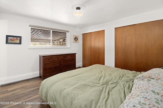 bedroom with multiple closets, baseboards, baseboard heating, and wood finished floors