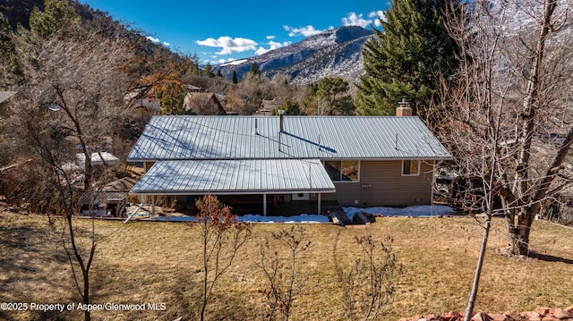 rear view of house featuring a chimney, a mountain view, metal roof, and a yard