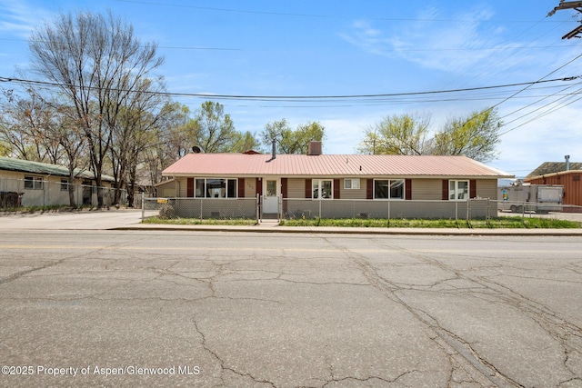 ranch-style home with a fenced front yard, a chimney, and metal roof