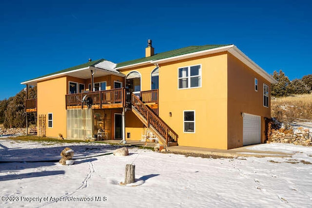 snow covered rear of property featuring a wooden deck and a garage