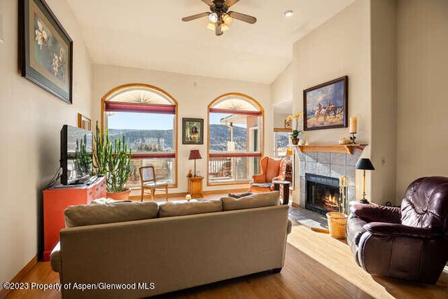 living room featuring a tiled fireplace, ceiling fan, lofted ceiling, and hardwood / wood-style flooring