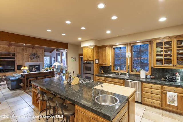 kitchen with backsplash, a center island with sink, a kitchen breakfast bar, sink, and light tile patterned flooring