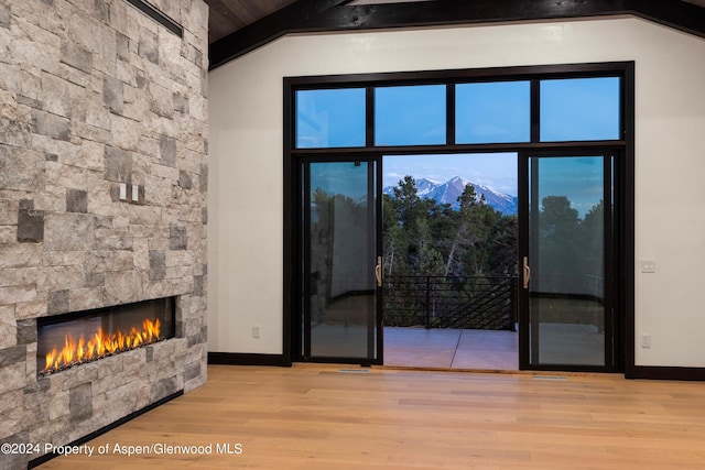 living room featuring a stone fireplace, a mountain view, light hardwood / wood-style floors, and lofted ceiling with beams