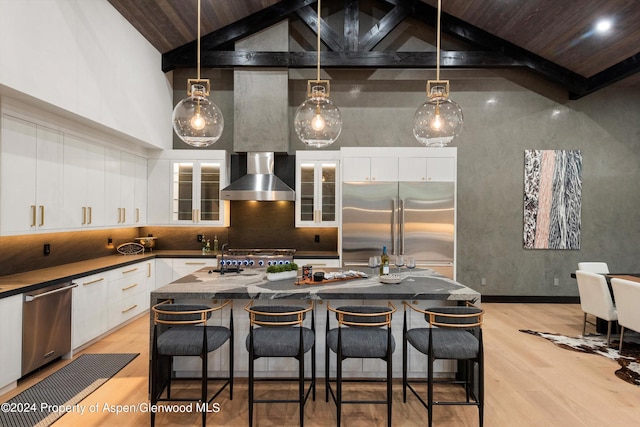 kitchen featuring wall chimney range hood, appliances with stainless steel finishes, tasteful backsplash, decorative light fixtures, and white cabinetry