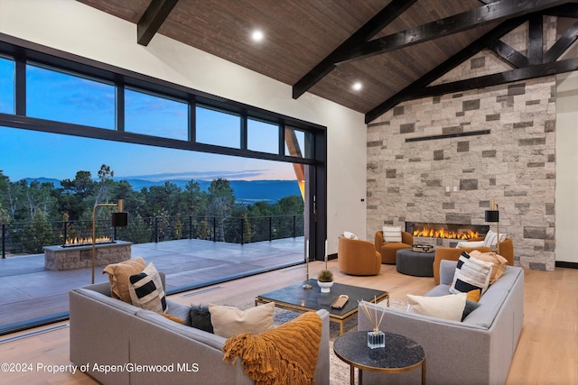 living room featuring wooden ceiling, high vaulted ceiling, light hardwood / wood-style floors, a fireplace, and beam ceiling