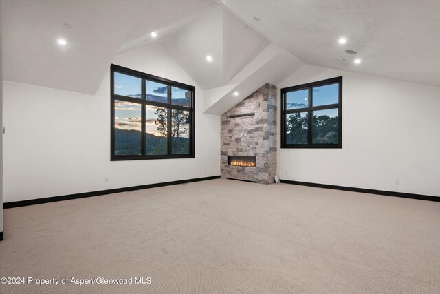 unfurnished living room with a stone fireplace, light colored carpet, and high vaulted ceiling