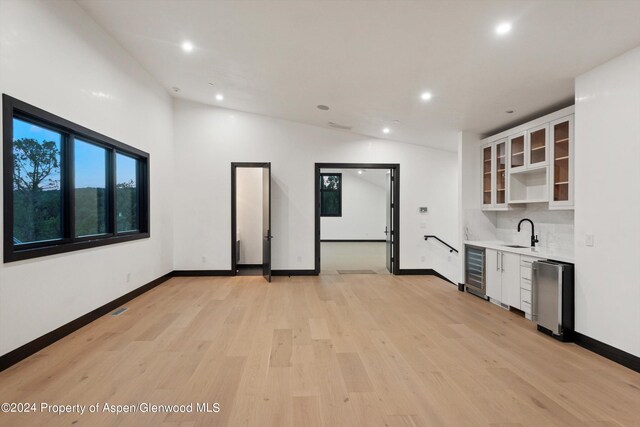 kitchen featuring lofted ceiling, wine cooler, light wood-type flooring, tasteful backsplash, and white cabinetry