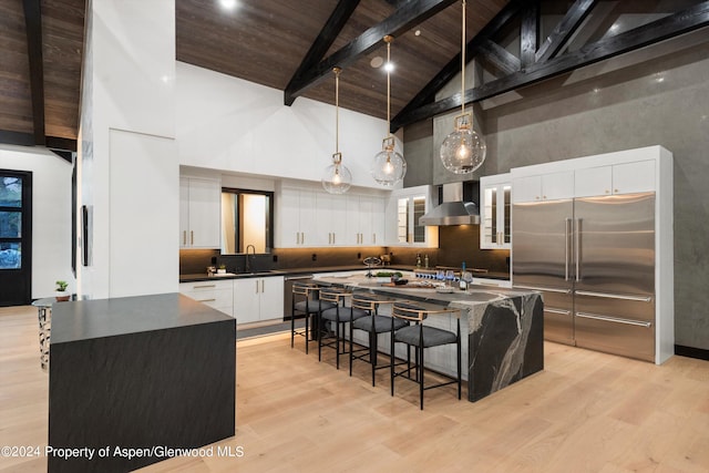 kitchen featuring appliances with stainless steel finishes, high vaulted ceiling, a kitchen island, and wall chimney exhaust hood