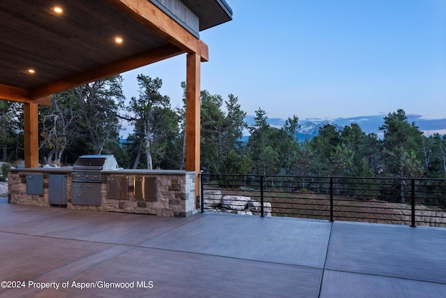 patio terrace at dusk featuring a grill, a mountain view, and exterior kitchen