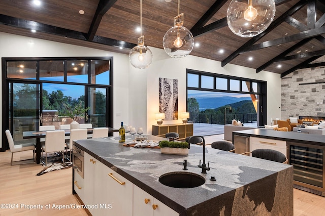 kitchen featuring white cabinets, wine cooler, hanging light fixtures, and dark stone counters