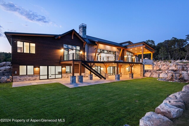 back house at dusk with a balcony, a yard, and a patio