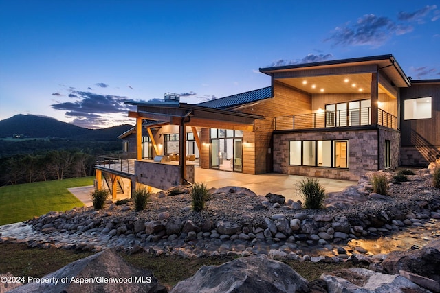 back house at dusk featuring a patio area, a mountain view, and a balcony