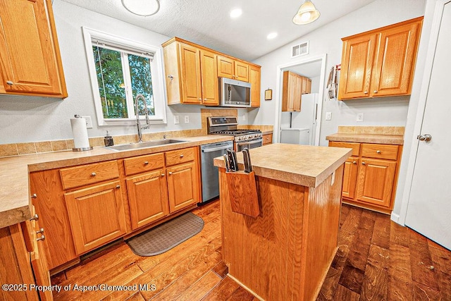 kitchen with dark hardwood / wood-style floors, a center island, lofted ceiling, appliances with stainless steel finishes, and sink