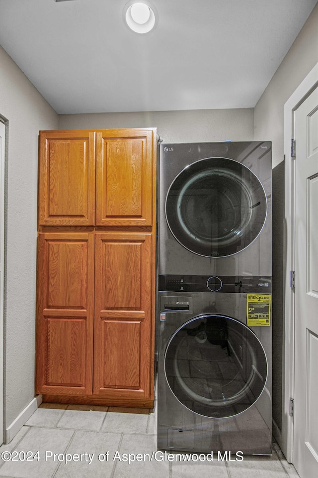 laundry room featuring cabinets, light tile patterned floors, and stacked washer and clothes dryer