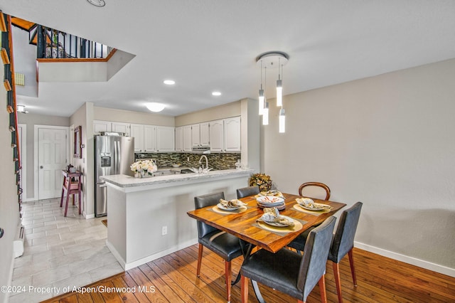 kitchen featuring white cabinetry, stainless steel fridge with ice dispenser, kitchen peninsula, decorative light fixtures, and decorative backsplash