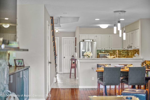 kitchen featuring kitchen peninsula, stainless steel refrigerator with ice dispenser, backsplash, pendant lighting, and white cabinetry