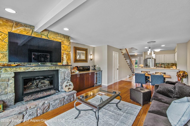 living room featuring beamed ceiling, light hardwood / wood-style floors, a fireplace, and beverage cooler