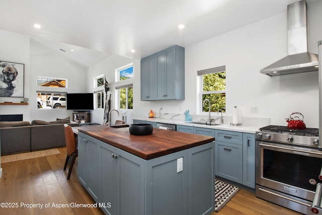 kitchen with stainless steel appliances, butcher block countertops, wall chimney exhaust hood, healthy amount of natural light, and lofted ceiling