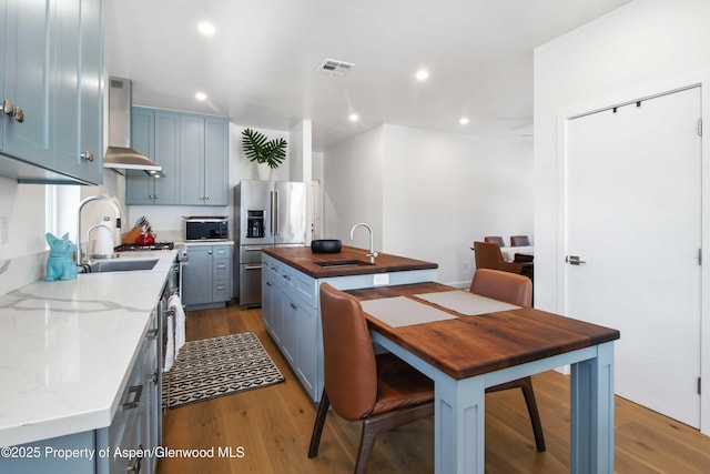 kitchen with stainless steel fridge, a sink, wall chimney exhaust hood, wood finished floors, and wood counters