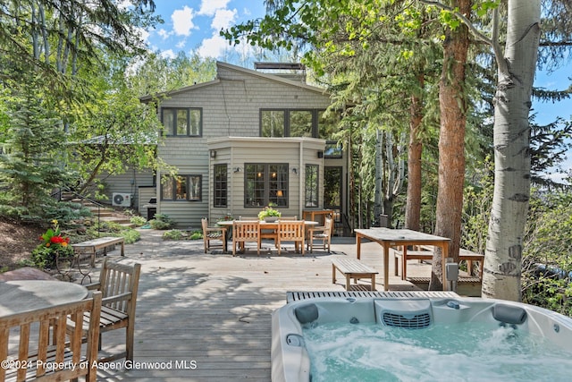 rear view of property with a wooden deck and an outdoor hot tub