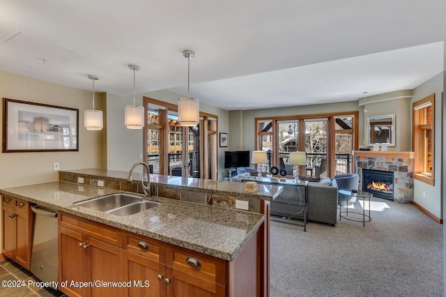 kitchen featuring dishwasher, sink, a stone fireplace, pendant lighting, and light carpet