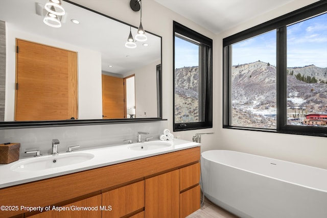 full bath with double vanity, a soaking tub, a mountain view, and a sink