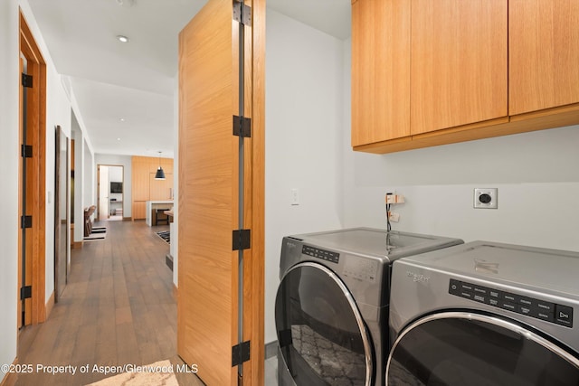 washroom with cabinet space, wood-type flooring, and washing machine and clothes dryer